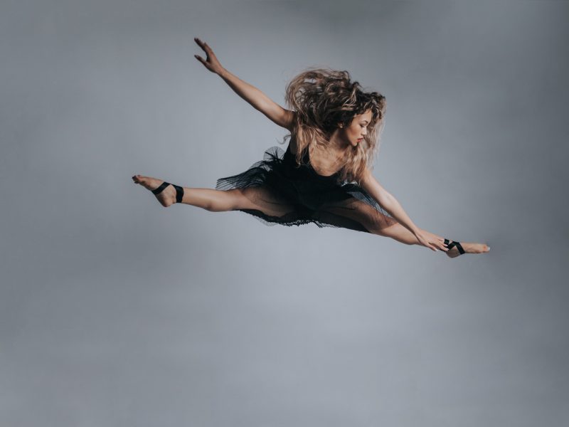Dance action photography in Melbourne - Female dancer mid air in split jump in black dress - barefoot